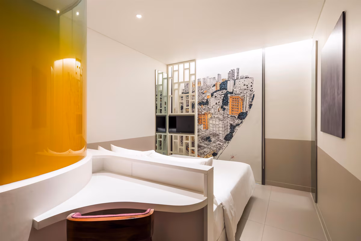 A compact hotel room with a bed, a window and storage built into the wall